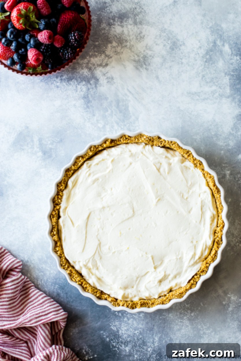 Vibrant Berry Tart 7 Overhead photo of a cream cheese whipped cream filled graham cracker crust with a bowl of colorful fresh berries off to the side, ready for assembly