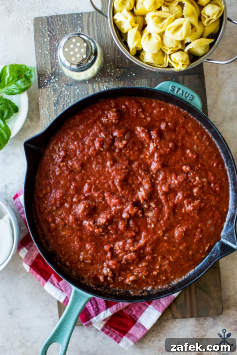 Cheesy Italian Sausage Tortellini Casserole 4 Italian sausage and chopped yellow onion cooking in a skillet, with a wooden spoon breaking up the sausage.
