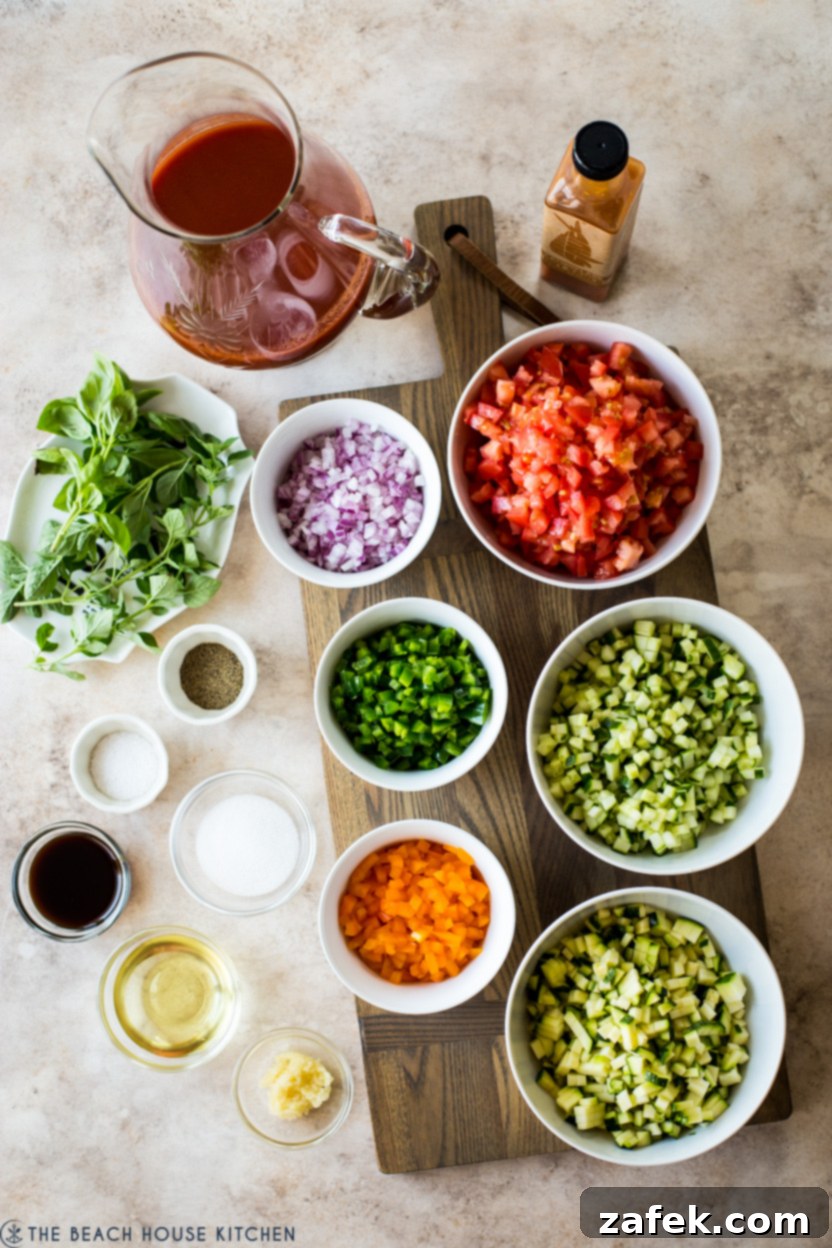 An overhead photo showcasing individual bowls of finely chopped gazpacho ingredients: tomatoes, cucumbers, peppers, onions, and basil.