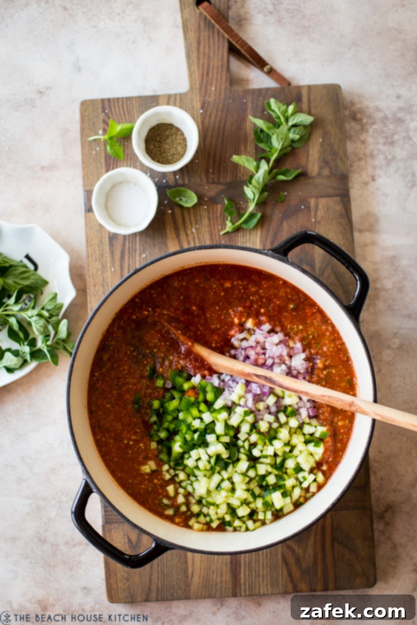 Overhead photo of a pot filled with gazpacho, topped with a colorful array of chopped vegetables and herbs.