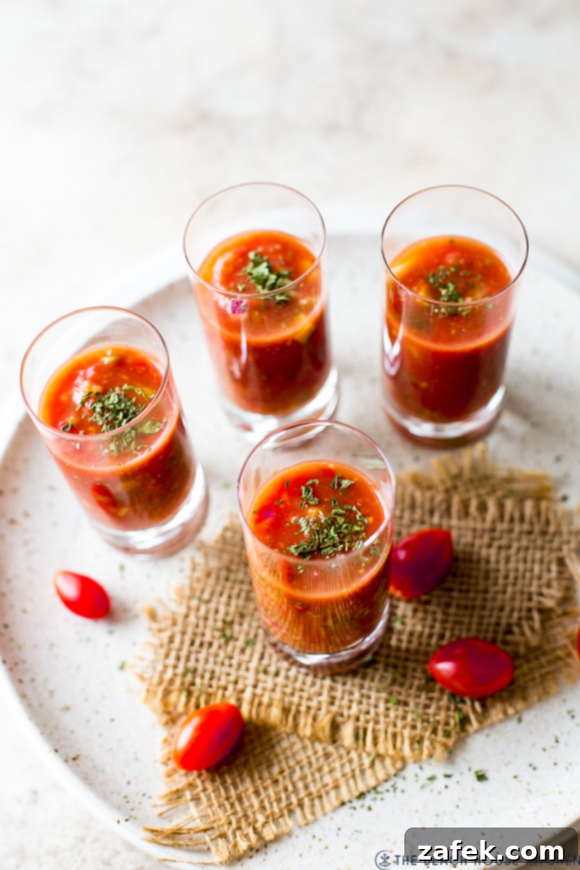 Four glass shooters meticulously arranged, each brimming with refreshing gazpacho, ready to be served.