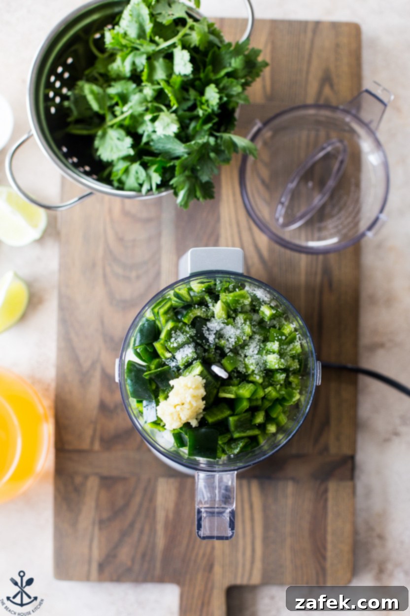 Overhead photo of a mini food processor filled with a vibrant green mixture of peppers, onion, garlic, parsley, and cilantro, ready to be blended for Arroz Verde.