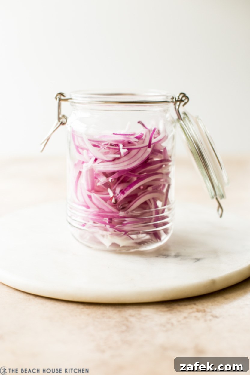 A clear glass jar filled with thinly sliced red onion rings, meticulously prepared for the pickling process