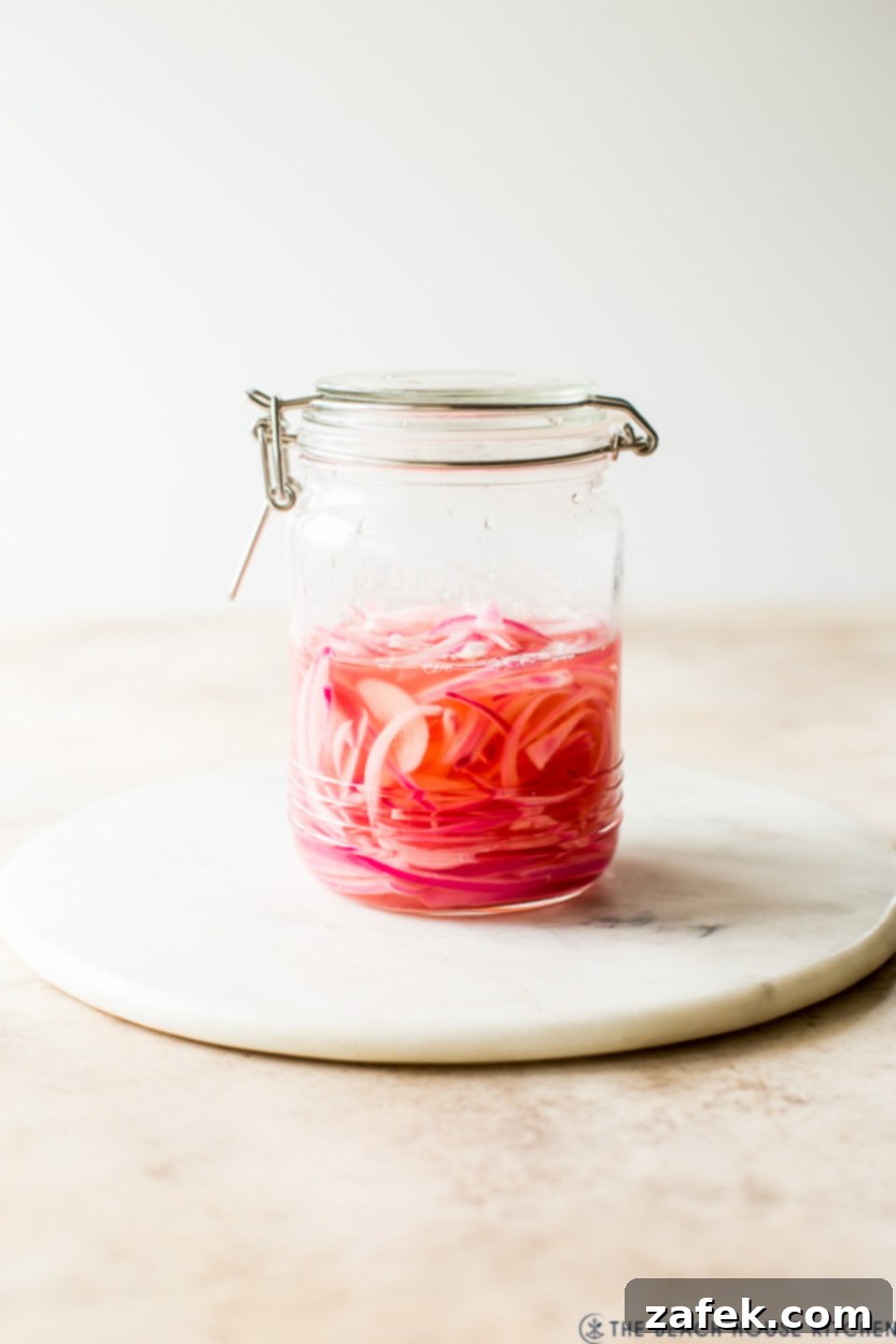 A beautifully presented glass jar of homemade pickled red onions, ready to serve, on a decorative round marble board