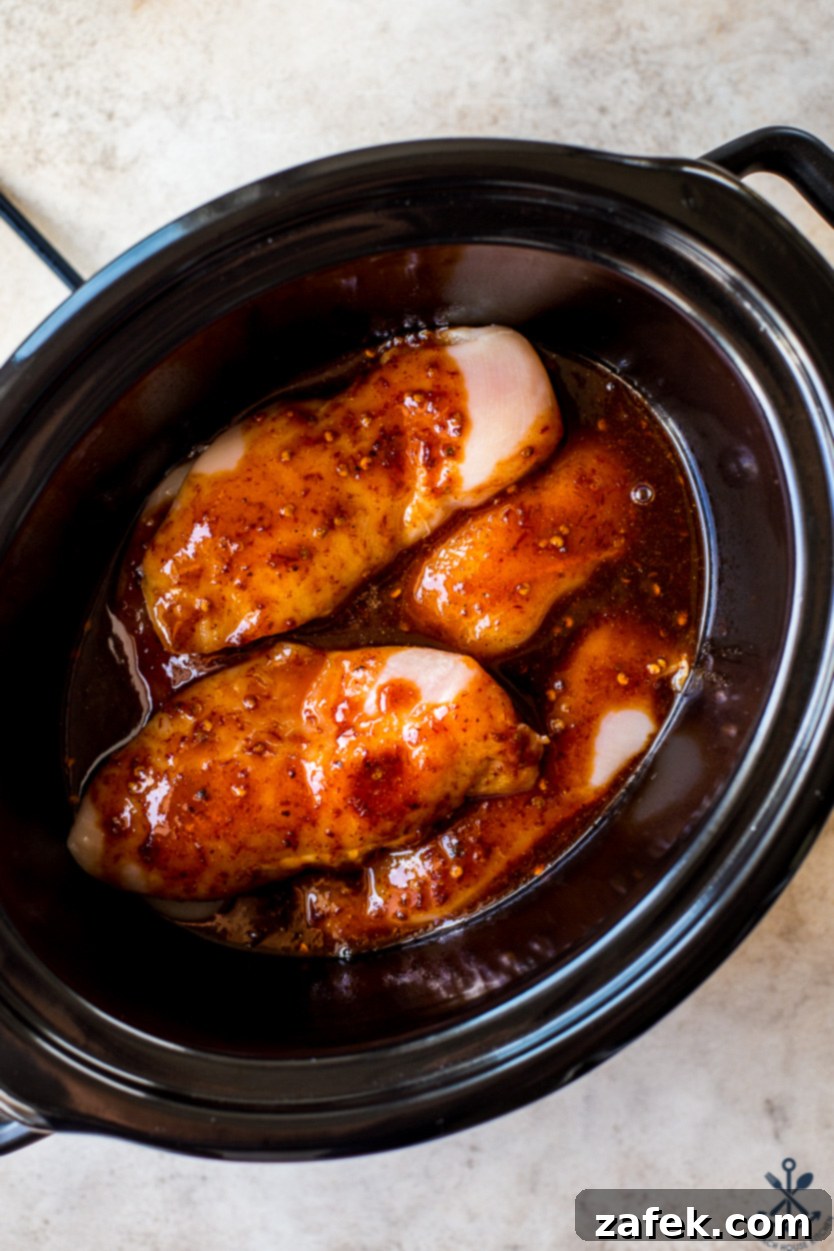Sticky Slow Cooker Honey Chipotle Chicken 5 Overhead photo of uncooked chicken breasts covered generously with a vibrant reddish-brown chipotle sauce, nestled inside a slow cooker before cooking