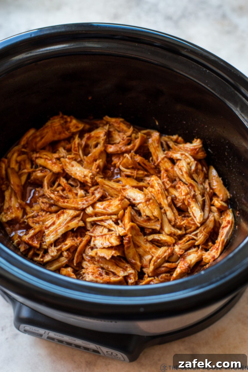 Overhead view of slow-cooked shredded honey chipotle chicken in a stoneware pot, showcasing its rich texture and appetizing color.