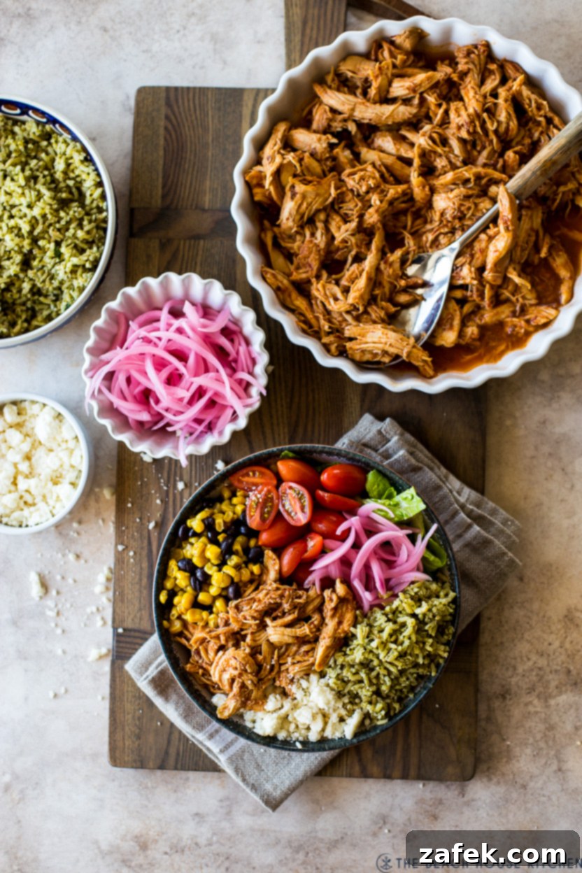 Overhead photo showing an assembled Honey Chipotle Chicken Bowl, a separate bowl of pickled red onions, and a large dish of shredded honey chipotle chicken.