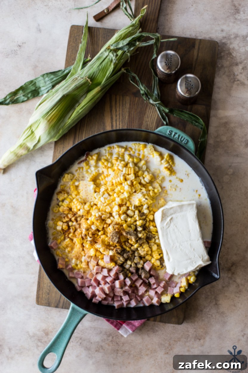 Overhead photo of a skillet filled with corn, ham, spices, milk and cream cheese