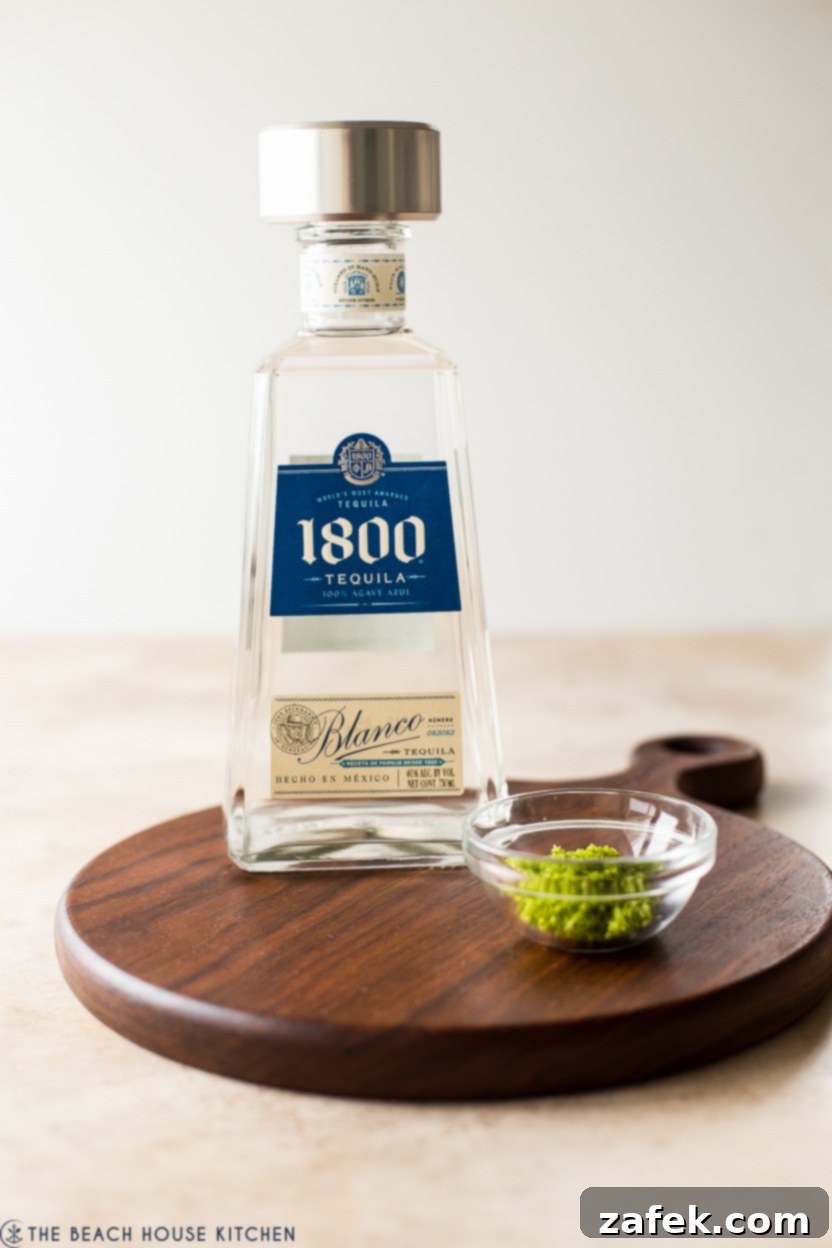 A bottle of smooth tequila positioned next to a small bowl brimming with vibrant green lime zest