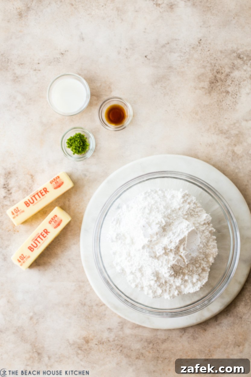 An overhead view of frosting ingredients featuring a bowl of sifted confectioners' sugar, two sticks of softened butter, and small bowls containing lime zest and vanilla extract