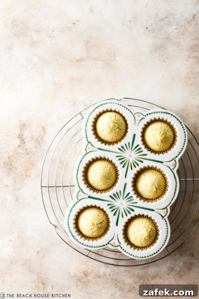 An overhead photo showing a cupcake pan filled with freshly baked, golden-yellow cupcakes, cooling down