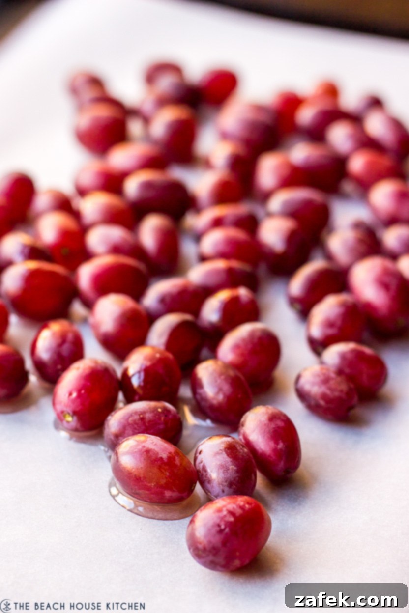 Maple Drizzled Roasted Grape Pear Blue Cheese Salad 4 Close-up photo of fresh red grapes arranged on a parchment-lined baking sheet, lightly drizzled with olive oil, ready for roasting.