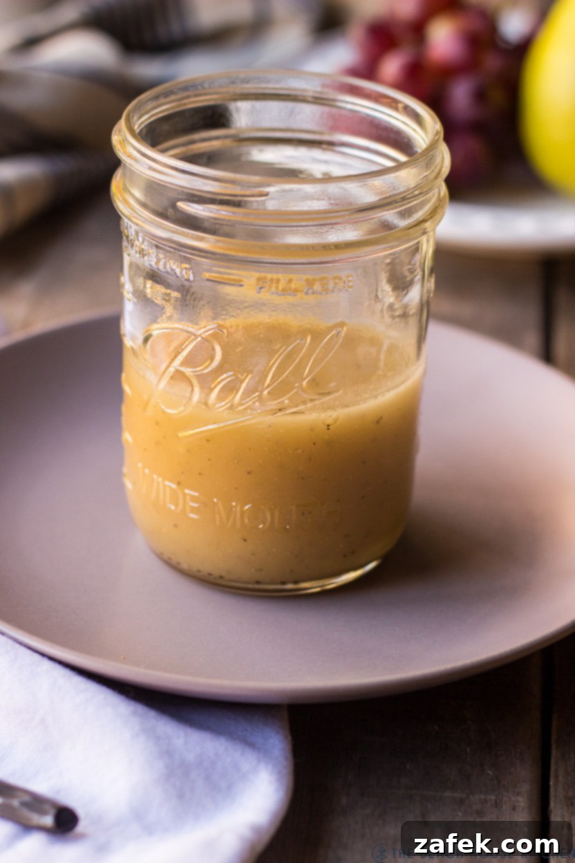 Maple Drizzled Roasted Grape Pear Blue Cheese Salad 5 A glass jar filled with the creamy, golden Maple Dressing, with a whisk resting beside it on a white plate, ready to be drizzled over the salad.