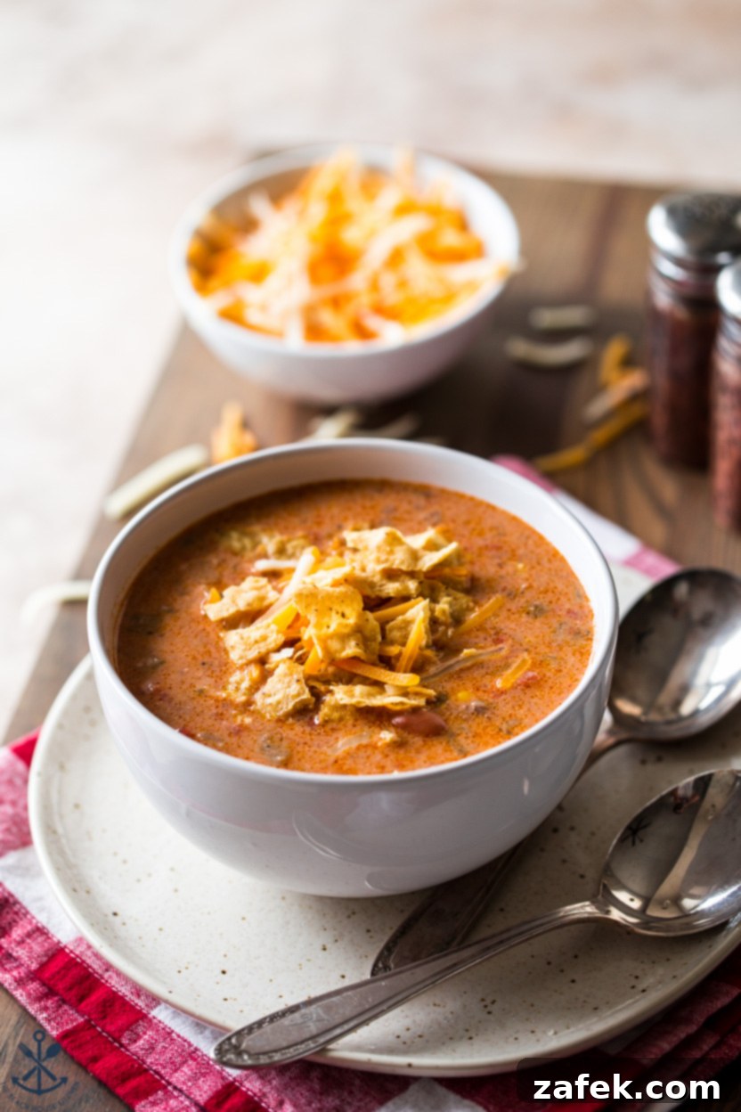 A bowl of slow cooker beef enchilada soup on a plate with two spoons