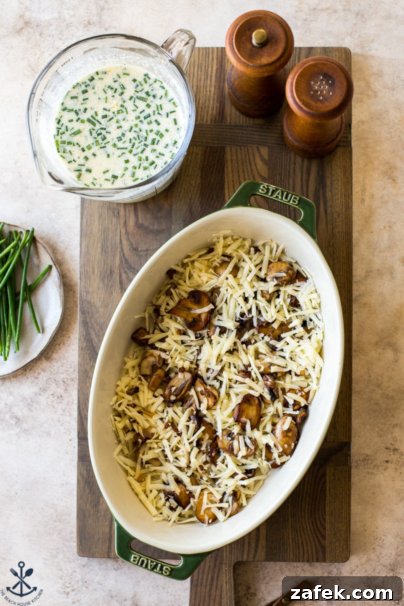 Savory Mushroom Cloud 7 Overhead photo of an oval baking dish filled with a base layer of shredded Gruyère cheese and sautéed mushrooms, before the custard is added
