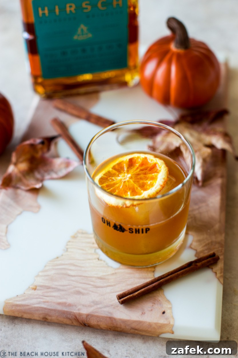 Fireside Pumpkin Old Fashioned 3 A close-up of a Pumpkin Spice Old Fashioned cocktail, garnished elegantly with a dehydrated orange slice, highlighting its rich amber hue.