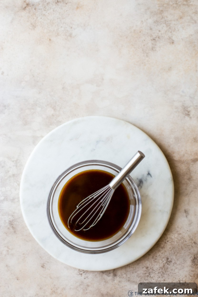 Fireside Pumpkin Old Fashioned 5 An overhead view of a rich, amber pumpkin spice syrup in a bowl, with a whisk resting beside it, indicating its readiness.