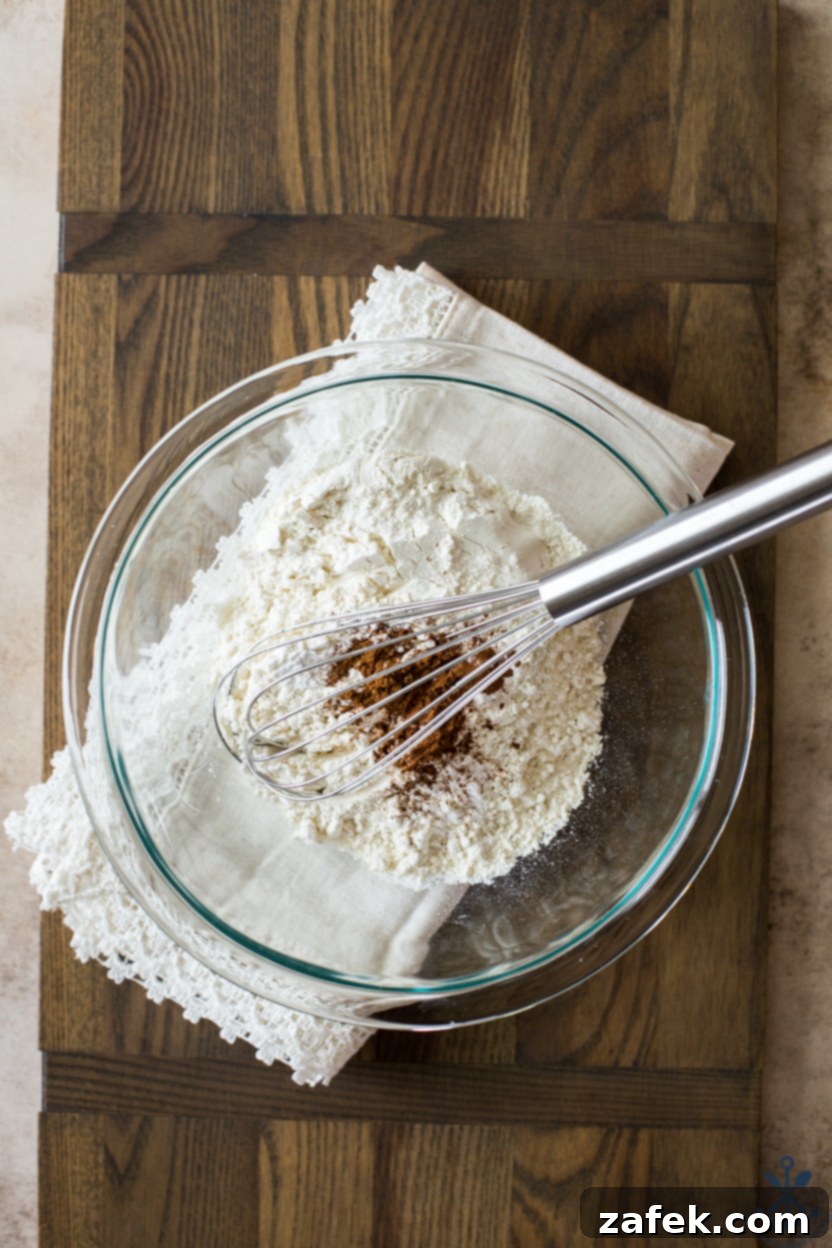 Overhead photo of a bowl filled with flour and cinnamon, with a silver whisk resting inside.
