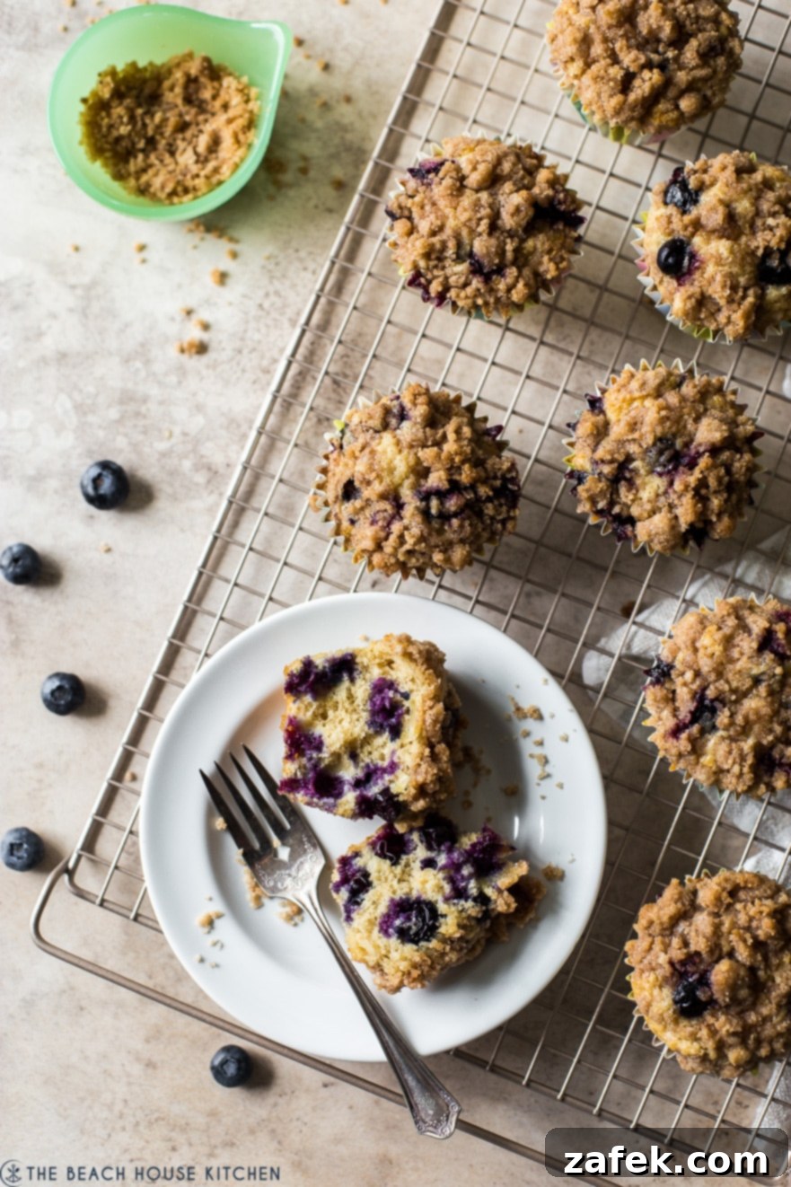 A close-up of a halved Bakery Style Blueberry Muffin on a white plate, showcasing its soft crumb and fruit-filled center