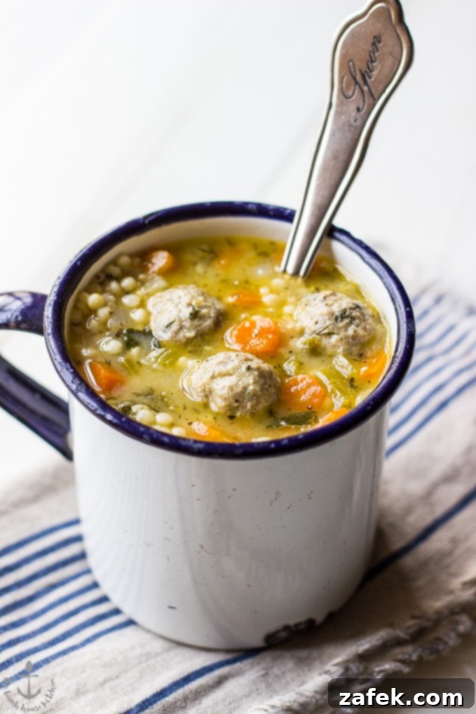 Italian Wedding soup in a white mug with a spoon, garnished with fresh herbs.