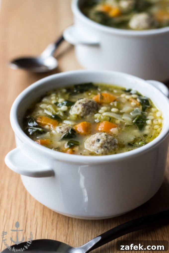 A close-up shot of a bowl of Italian Wedding Soup, showing the meatballs, pasta, and vegetables.
