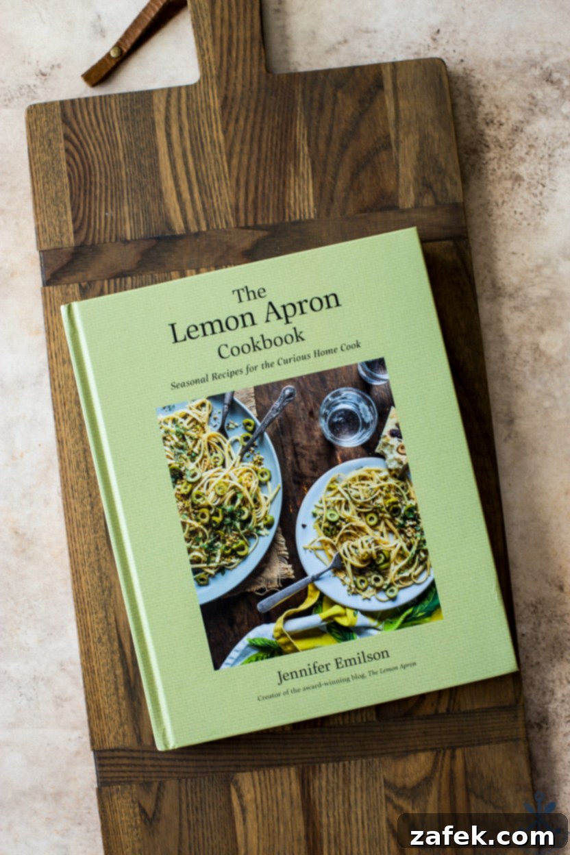 A Taste of Home: Mum's Chicken and Rice 4 Overhead photo of The Lemon Apron Cookbook, a hardcover book with an inviting cover design, resting on a rustic wooden board, ready for exploration.
