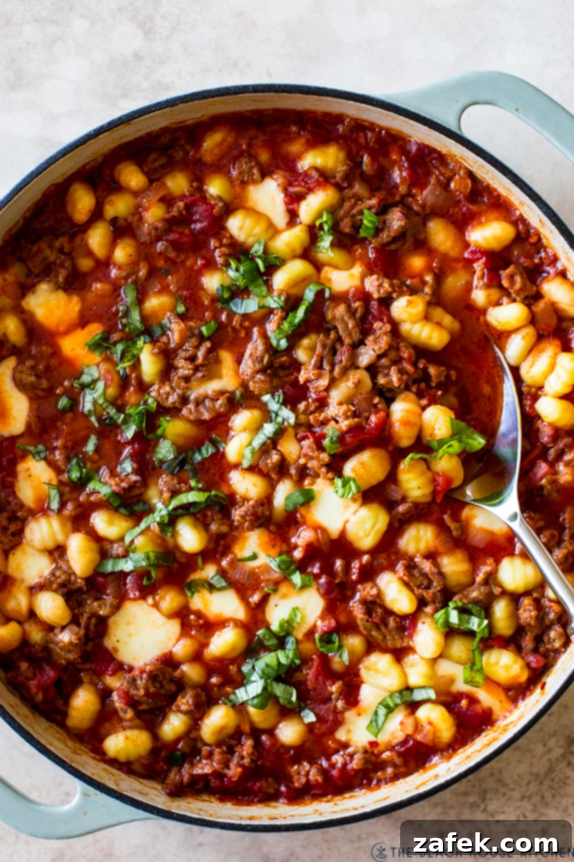 Up close overhead photo of a skillet of a gnocchi dish with sausage and red sauce, garnished with fresh basil.