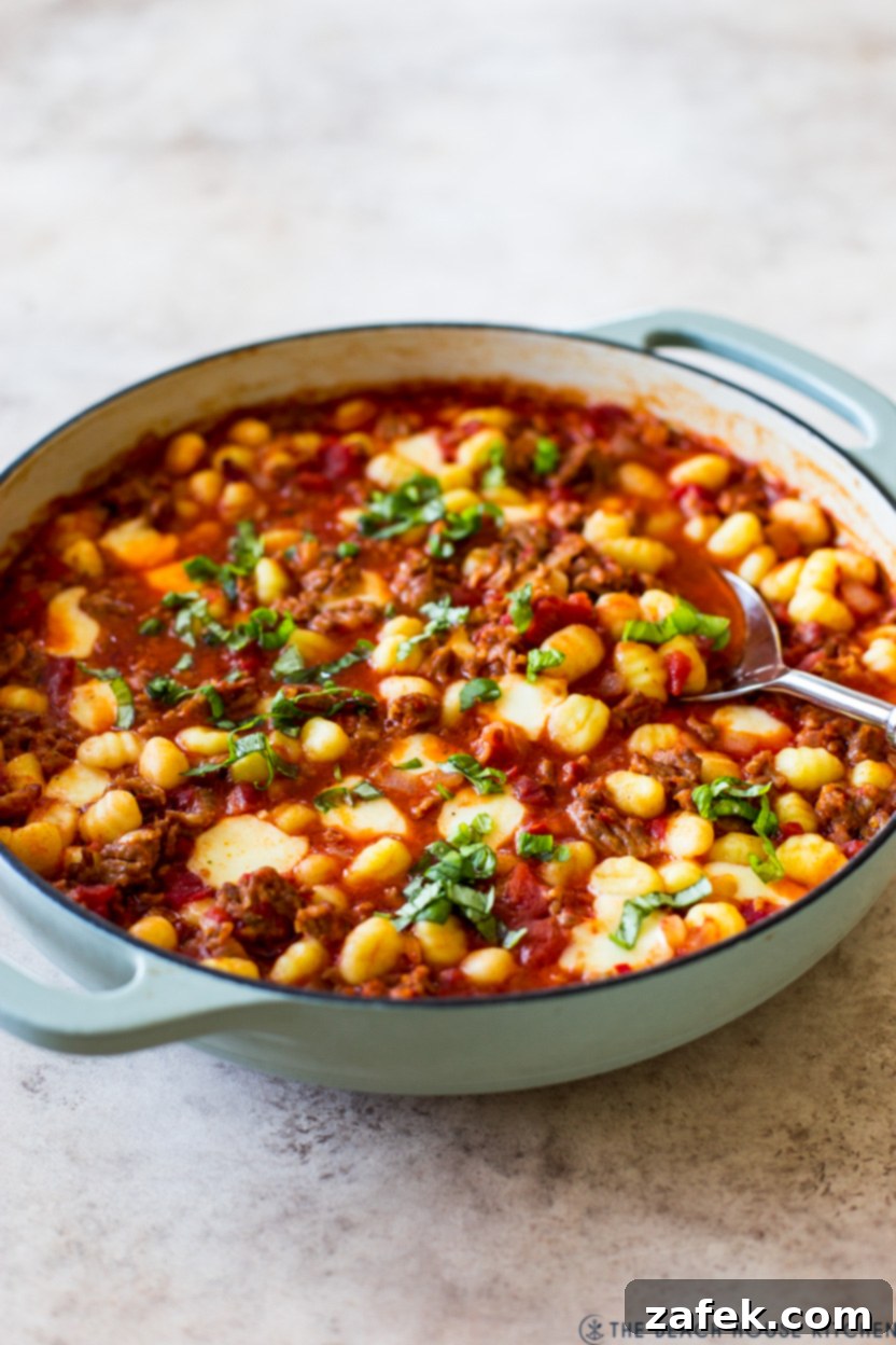 A skillet of Italian sausage and gnocchi amatriciana, fresh from the oven, with melted cheese and bubbling sauce.