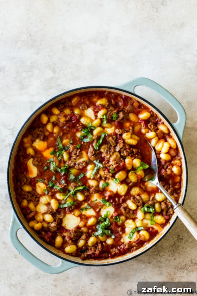 Overhead photo of a skillet of pasta, sausage, and red sauce, simmering on the stove.