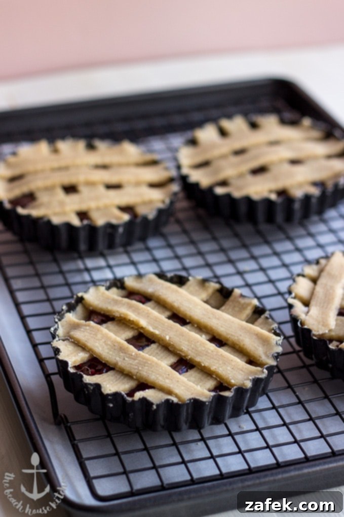 Miniature Linzer Torte on a wire rack cooling, with more in the background.