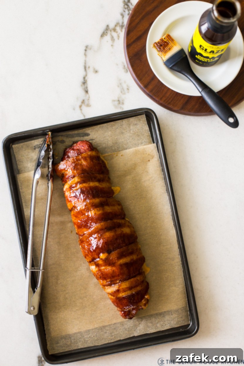 Exquisite Bacon-Wrapped Stuffed Pork Tenderloin 3 Overhead photo of an uncooked bacon wrapped stuffed pork tenderloin resting on a baking sheet before roasting