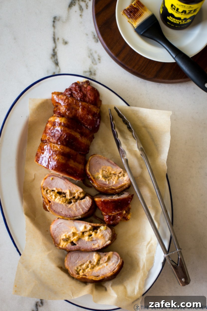 Exquisite Bacon-Wrapped Stuffed Pork Tenderloin 8 Overhead photo of a beautifully sliced bacon wrapped stuffed pork tenderloin on an oval platter, showcasing the creamy, cheesy filling
