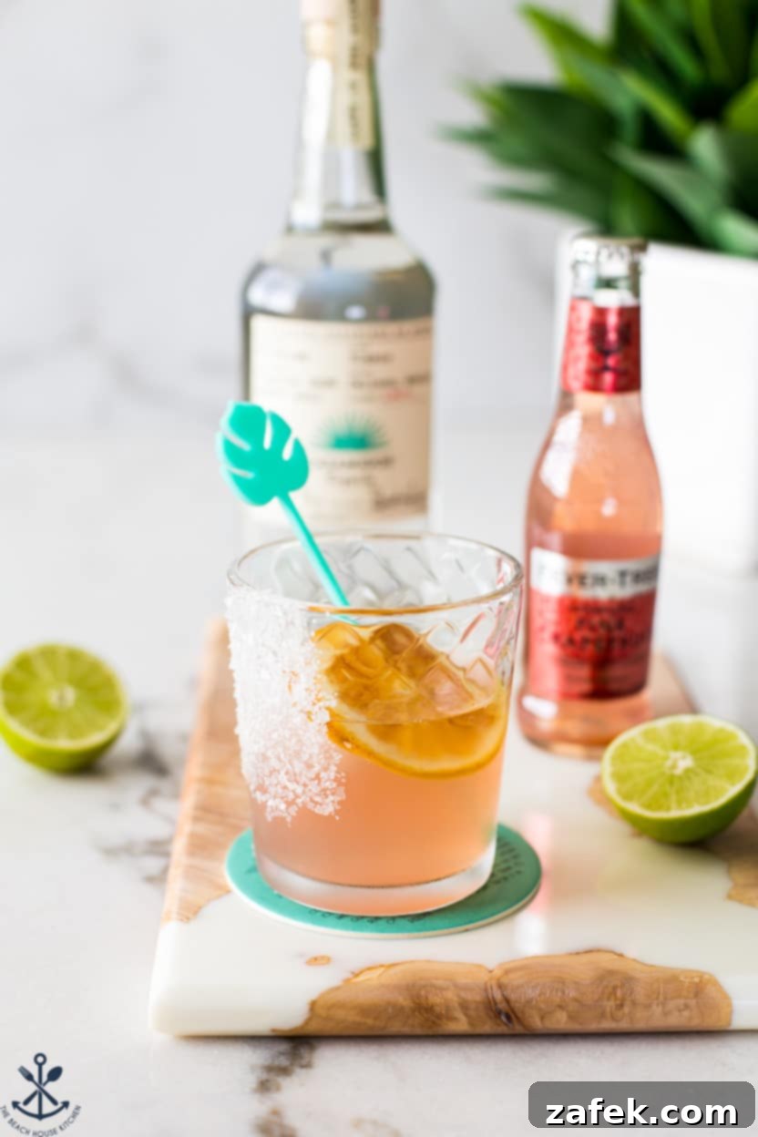 The Perfect Paloma Cocktail 2 A Paloma cocktail on a board with a green palm leaf stirrer, showcasing a vibrant pink drink.