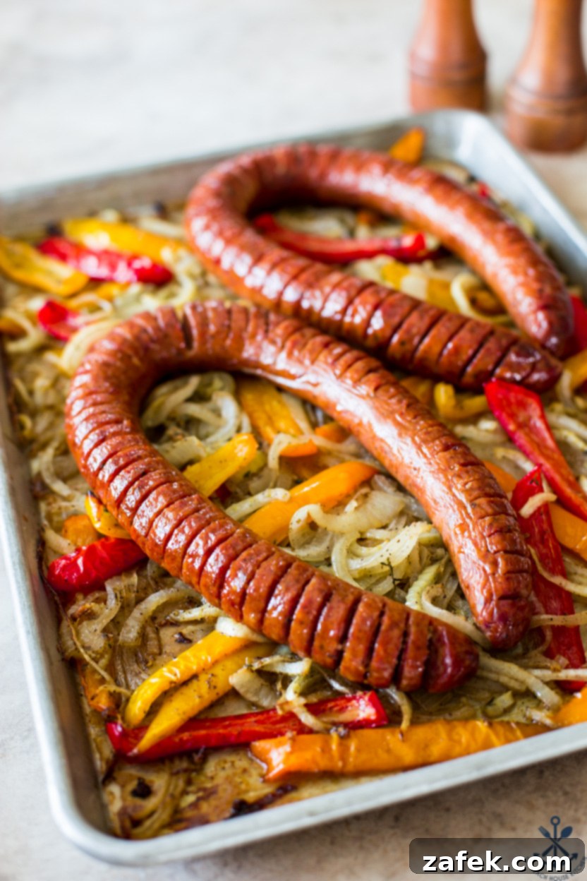 A vibrant sheet pan filled with golden-brown Hasselback Kielbasa surrounded by perfectly roasted onions and colorful bell peppers.