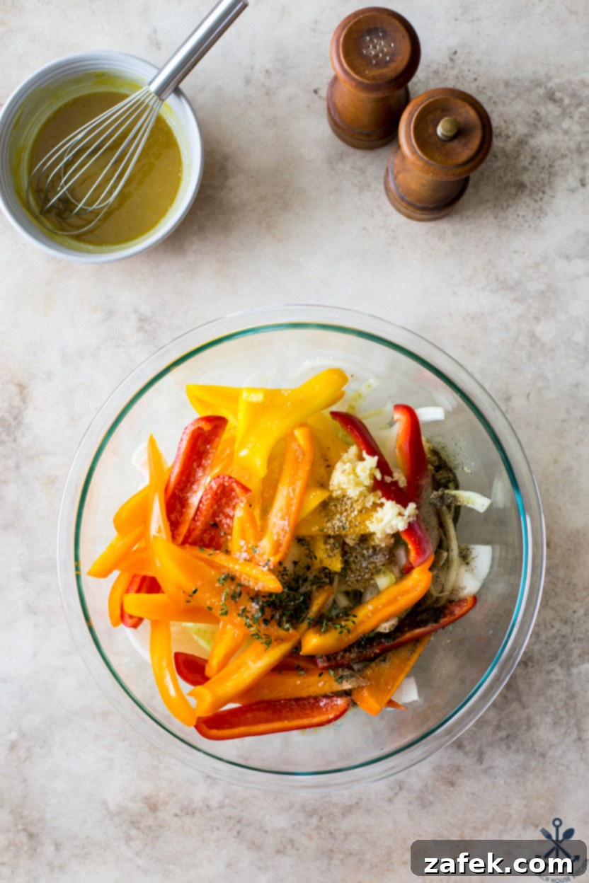 A close-up view of a large mixing bowl filled with a colorful medley of sliced onions, bell peppers, minced garlic, and various aromatic spices, all tossed and ready for the sheet pan.