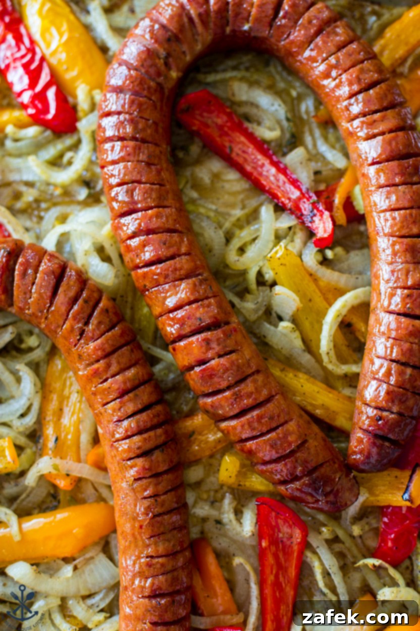 An artistic, up-close overhead shot of the completed sheet pan meal, showcasing the detailed cuts of the Hasselback kielbasa, the rich glaze, and the vibrant roasted vegetables.