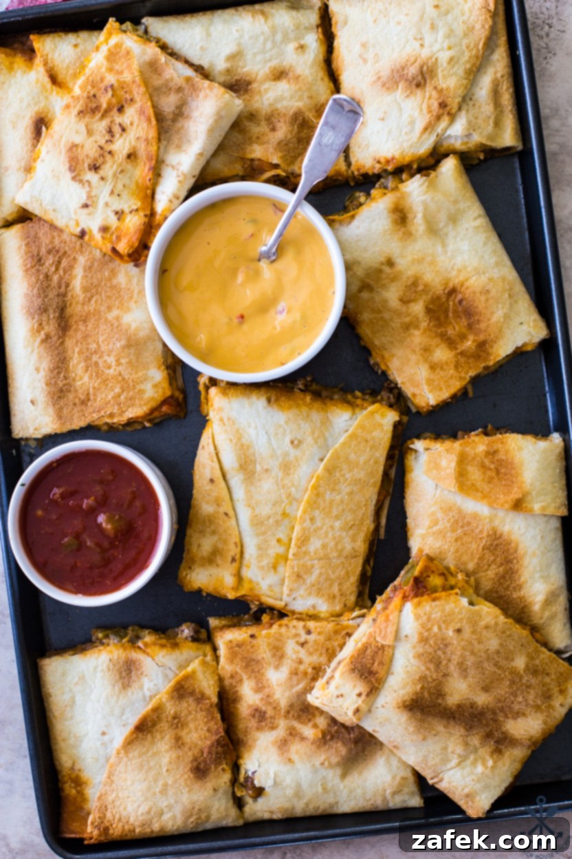 Overhead photo of a large sheet pan of freshly baked, neatly sliced beef quesadillas, beautifully garnished with fresh cilantro and ready to be served with dipping sauces