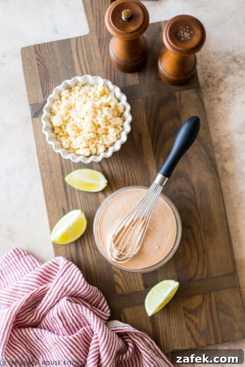 Overhead photo of creamy dressing in a small bowl with a whisk and a small bowl of crumbled Cotija cheese
