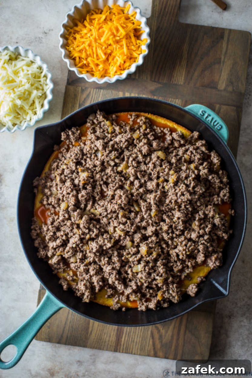 Southwest Tamale Bake 9 Overhead photo of a skillet filled with cooked ground beef, with two separate bowls of shredded cheeses (cheddar and Monterey Jack) off to the side, ready for topping