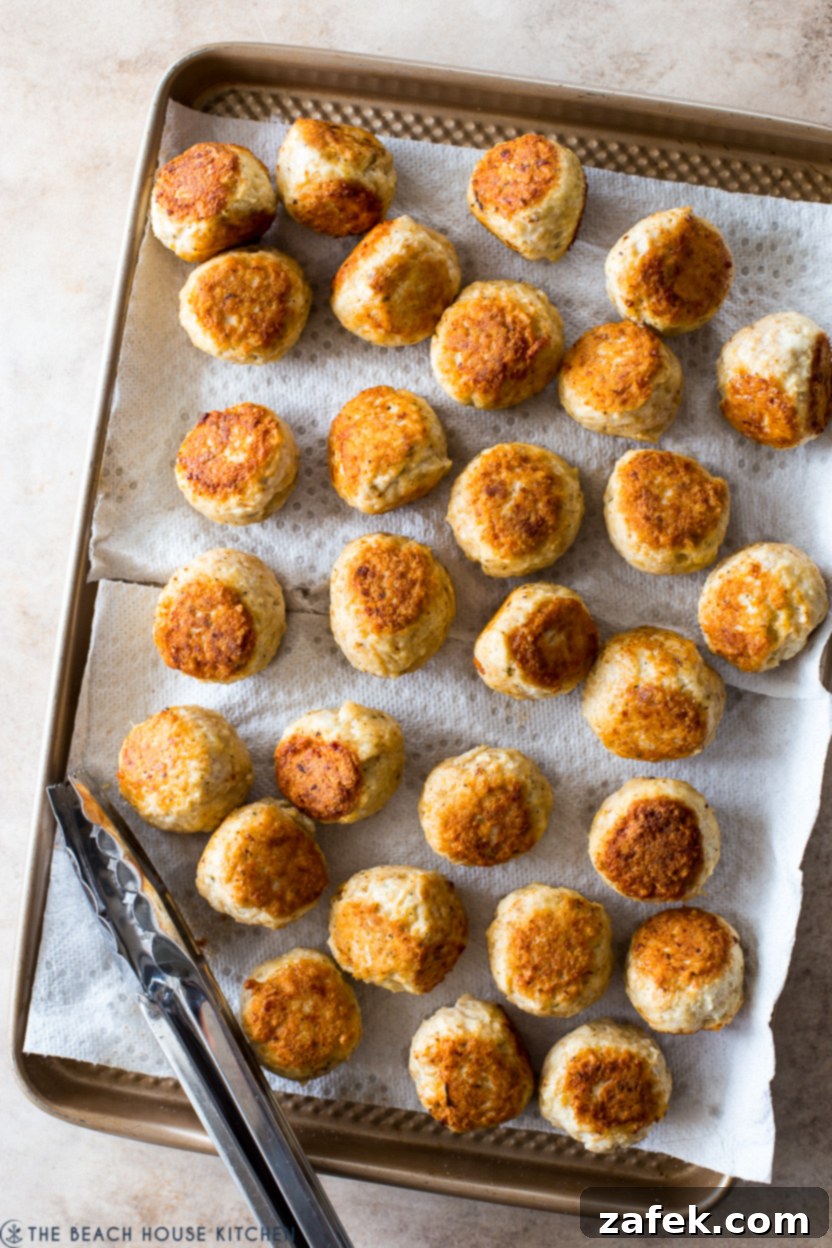 Golden-brown chicken piccata meatballs searing in a hot skillet with olive oil, ready to be flipped.