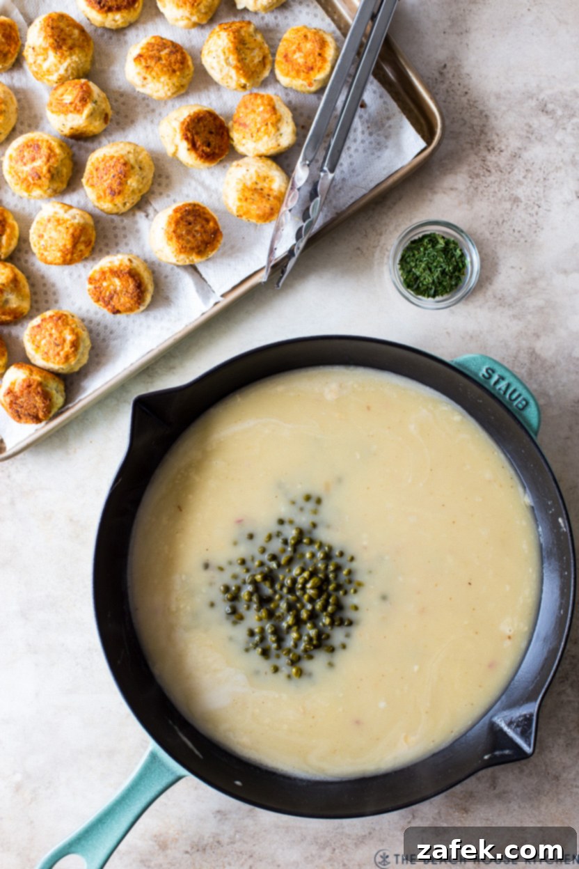 Finished chicken piccata meatballs simmering in the creamy lemon-caper sauce in a skillet, ready to serve.