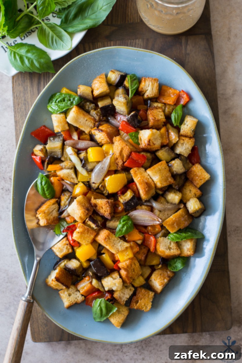 Overhead photo of a prepared Sheet Pan Roasted Vegetable Panzanella on a blue oval plate, ready to serve.