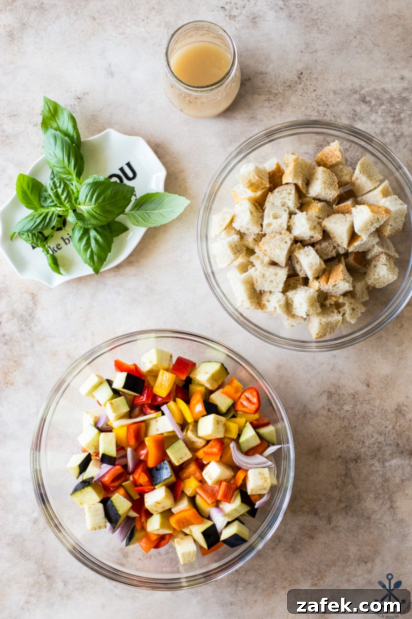 Overhead photo of the uncooked ingredients for Sheet Pan Roasted Vegetable Panzanella spread out on a baking sheet, ready for the oven.