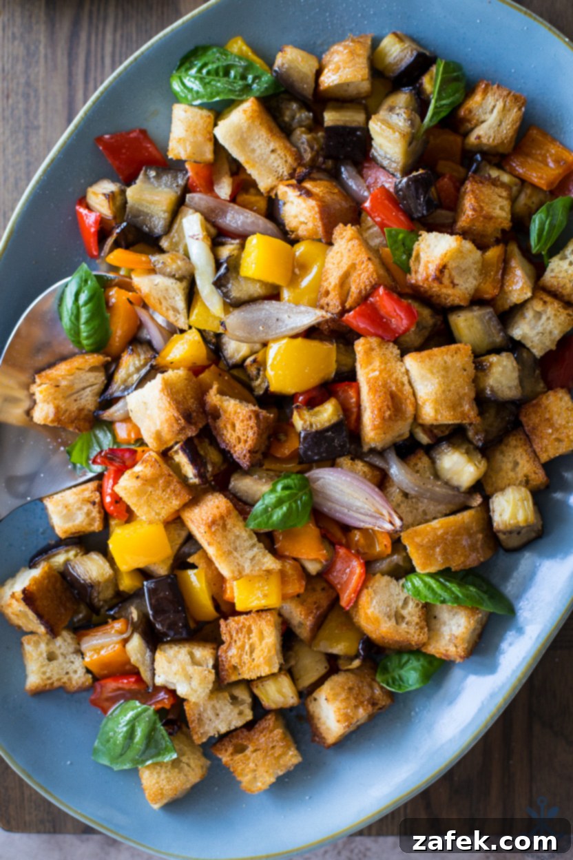 Up close overhead photo of a panzanella salad on a blue oval platter, showcasing the crispy bread, roasted vegetables, and fresh basil.