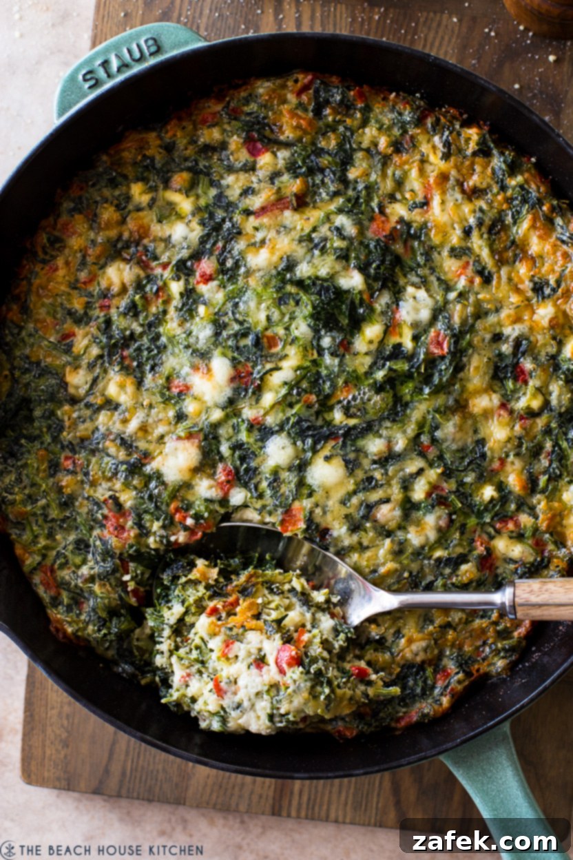 Up close overhead photo of a cheesy Greek Egg Bake with Spinach, loaded with feta, cheddar, spinach and roasted red peppers.