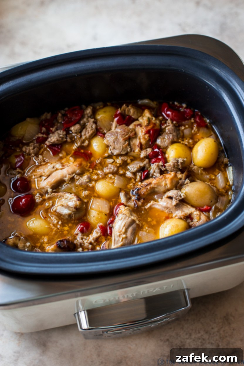 A slow cooker filled with golden-brown chicken scarpariello with sausage, potatoes, and peppers