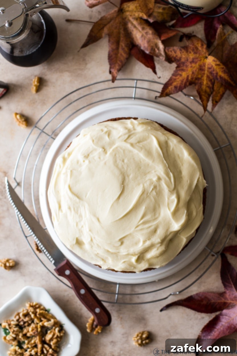 Maple Walnut Cake 3 Overhead photo of a cream cheese frosted maple walnut cake on a plate on a round wire rack surrounded by fall leaves