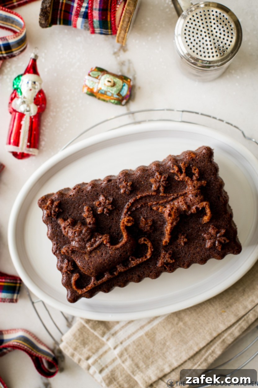 Overhead photo of a holiday gingerbread loaf on an oval white plate, dusted with confectioners' sugar