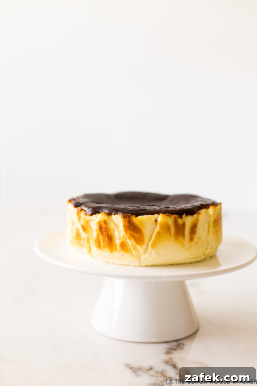 Perfect Air Fryer Basque Cheesecake 2 A beautifully burnt Basque cheesecake resting on a pristine white cake pedestal, ready to be served, highlighting its rich, creamy interior and dark, caramelized top.