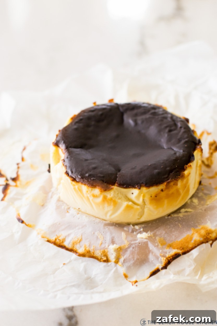 Perfect Air Fryer Basque Cheesecake 4 A close-up view of a slice of Air Fryer Basque cheesecake, showcasing its burnt top and the smooth, creamy interior texture, served on a piece of white parchment paper.